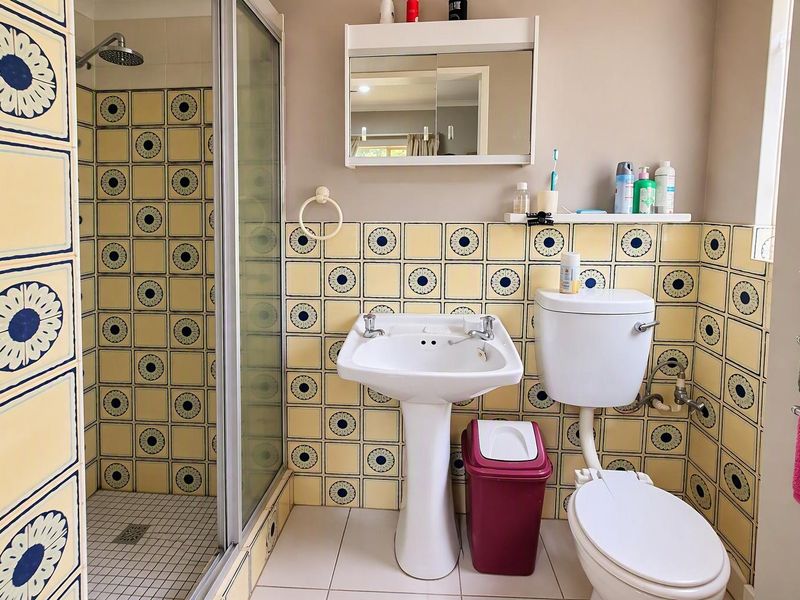 A functional bathroom featuring a pedestal basin, toilet, and a separate shower enclosure with decorative tiled walls and flooring.