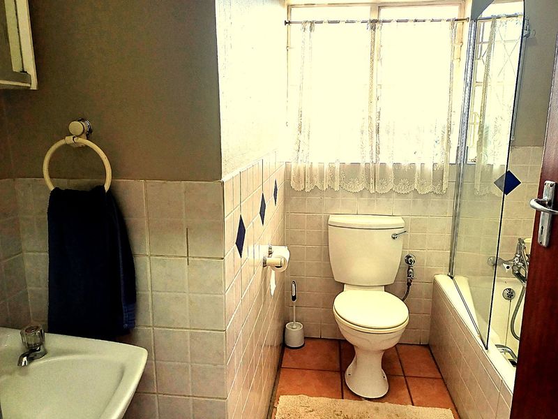 A functional bathroom featuring a built-in bathtub with a glass screen, pedestal basin, and toilet, finished with classic wall and floor tiling.