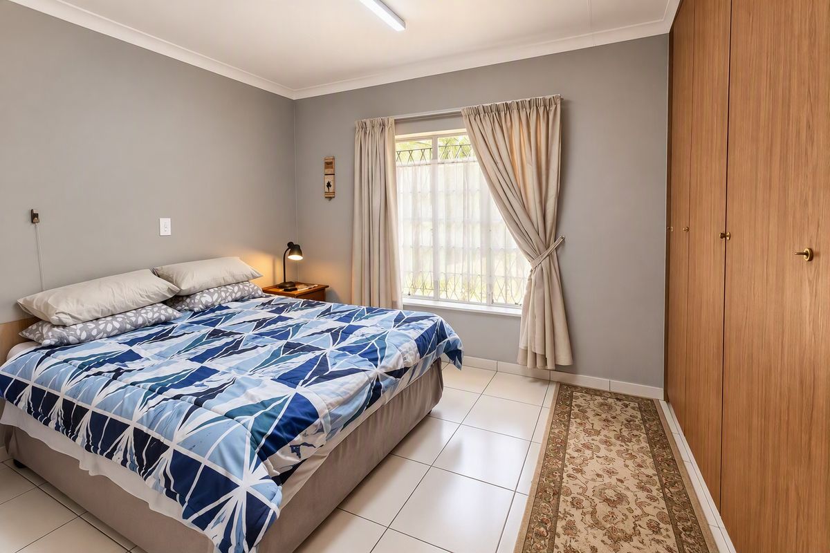 A well-maintained bedroom featuring neutral grey walls, tiled flooring, and ample built-in cupboard storage with natural light from the window.