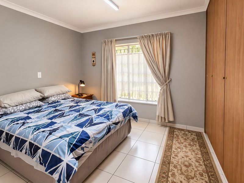 A well-maintained bedroom featuring neutral grey walls, tiled flooring, and ample built-in cupboard storage with natural light from the window.