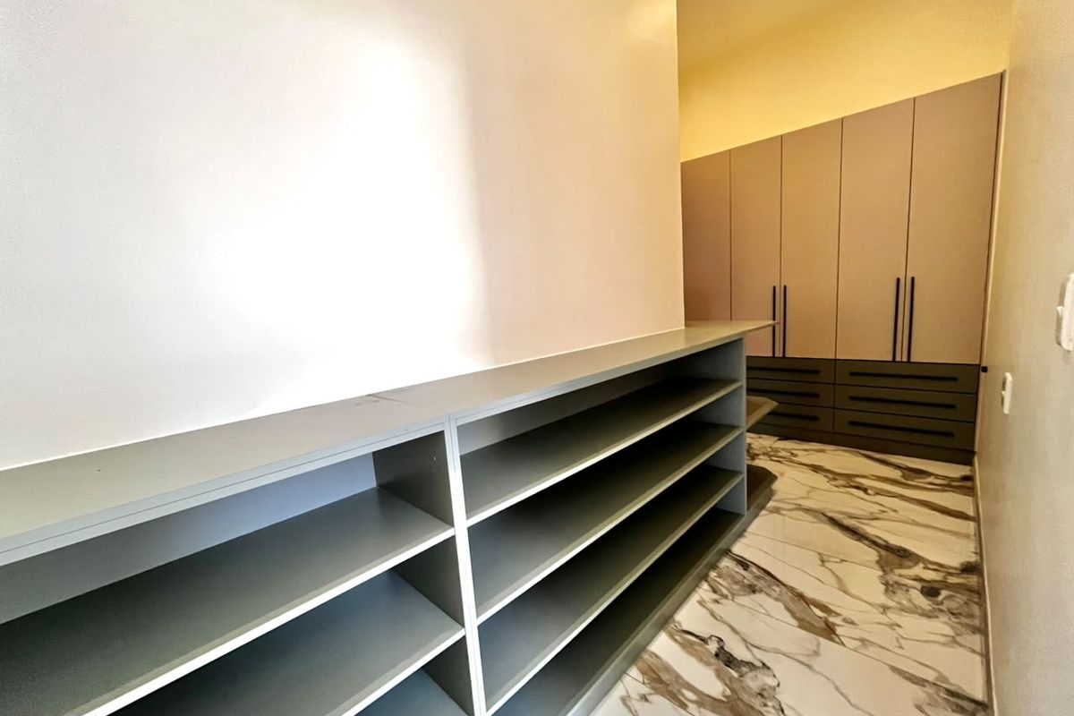 A clean, modern bedroom area featuring extensive built-in cabinetry, shelving units, and elegant marble-look floor tiles.