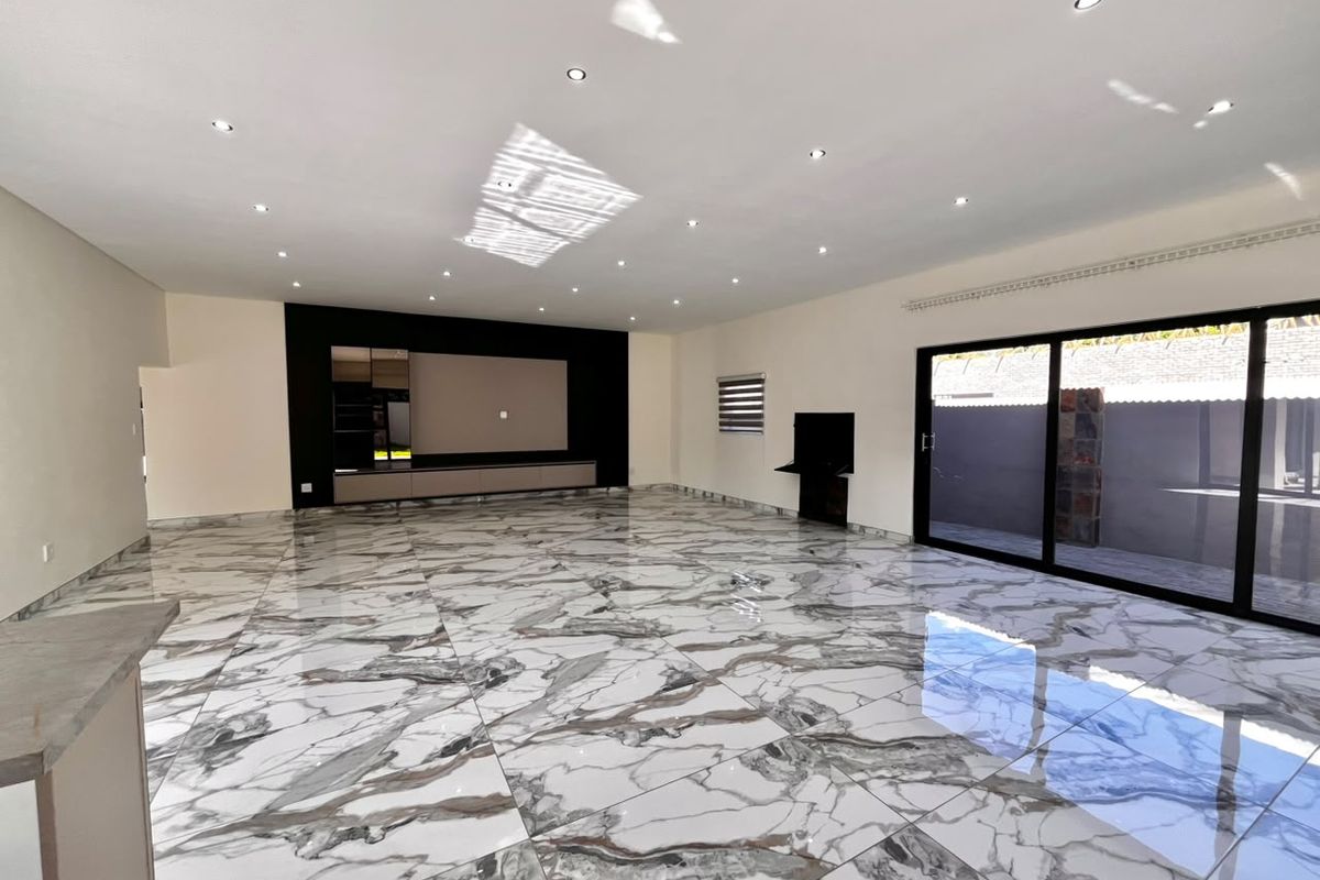 Spacious, modern living area featuring high-gloss marble-look floor tiles, recessed downlighting, and large sliding glass doors leading to the patio.
