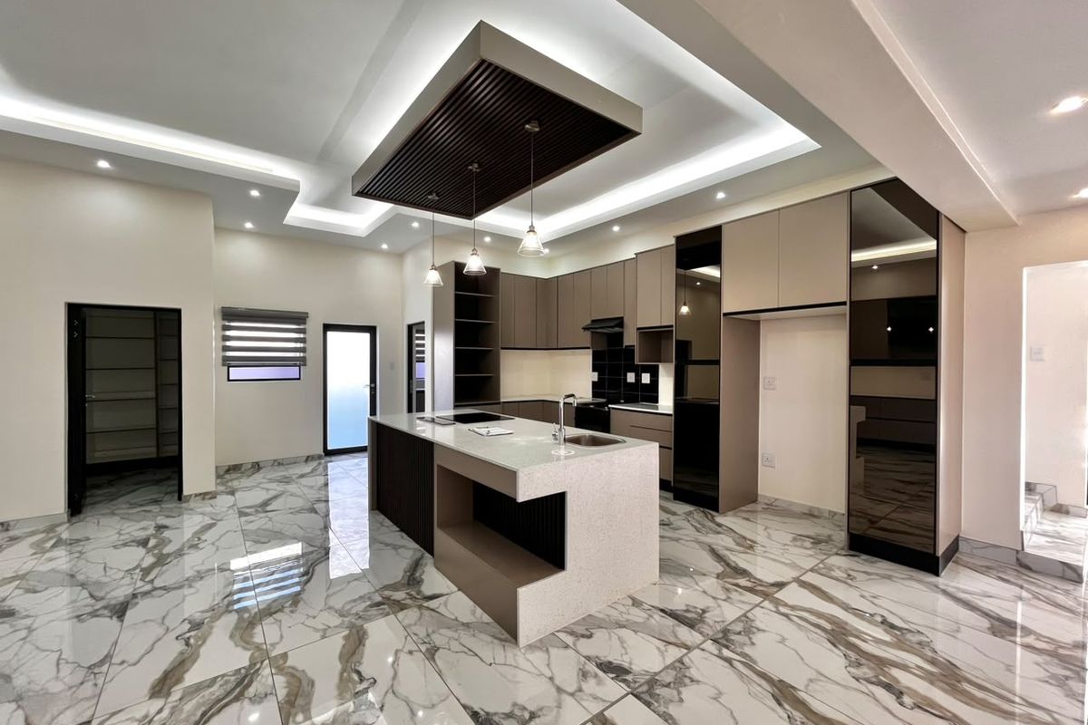 Modern, high-end kitchen featuring a central island with stone countertops, custom cabinetry, integrated appliances, and sophisticated recessed ceiling lighting with marble-look flooring.