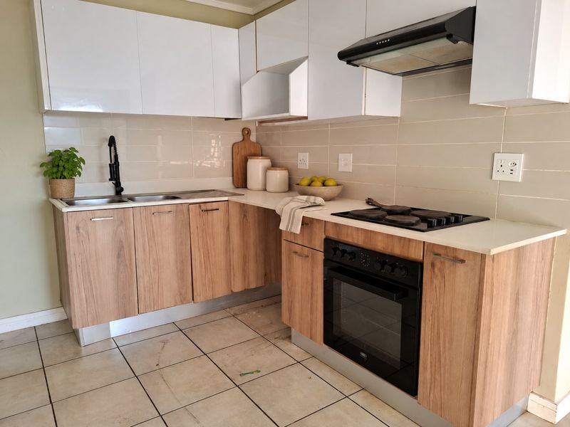 A functional kitchen featuring wood-look lower cabinetry, white upper cabinets, integrated oven and hob, and a tiled backsplash.