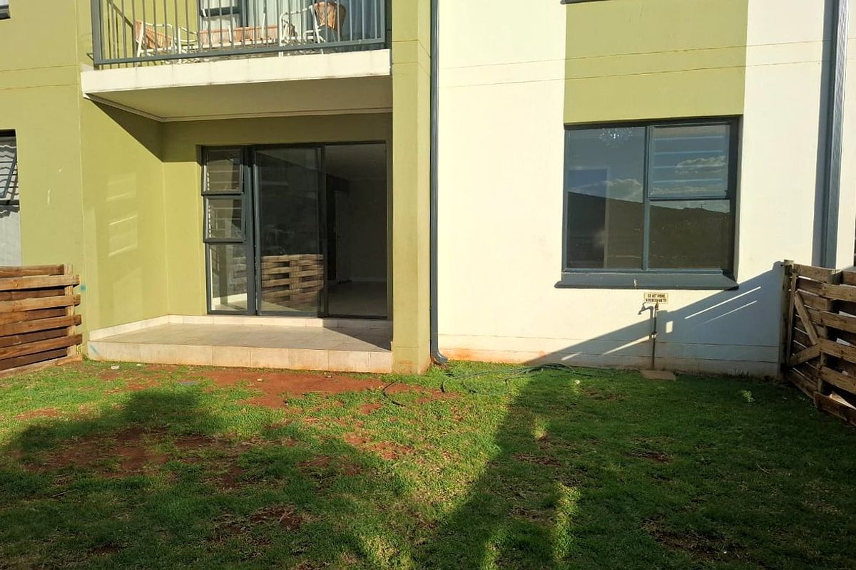 Rear view of an apartment featuring a small tiled patio, a private garden area with wooden fencing, and an upper-level balcony.