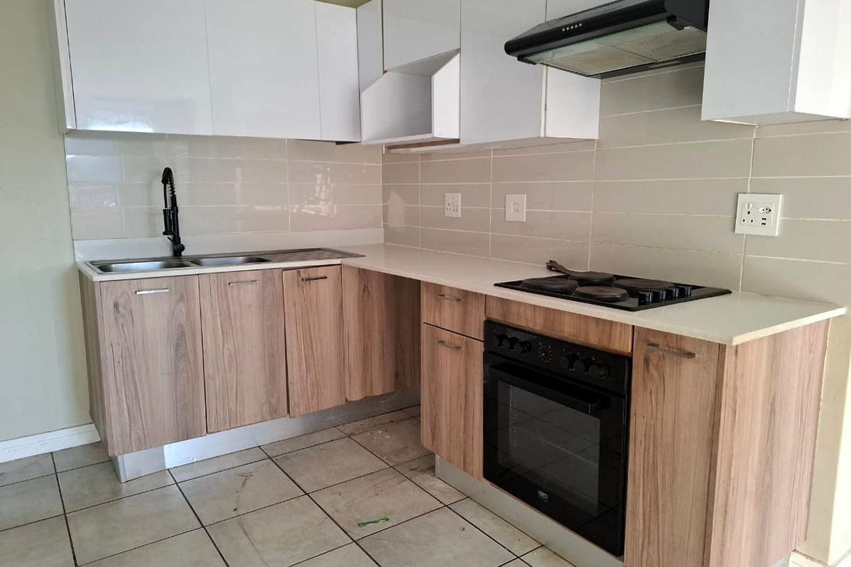 Modern kitchen featuring wood-grain lower cabinetry, white upper cabinets, stone countertops, built-in oven, electric hob, and extractor fan.