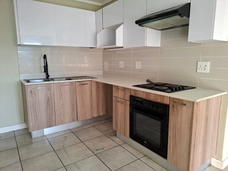 Modern kitchen featuring wood-grain lower cabinetry, white upper cabinets, stone countertops, built-in oven, electric hob, and extractor fan.