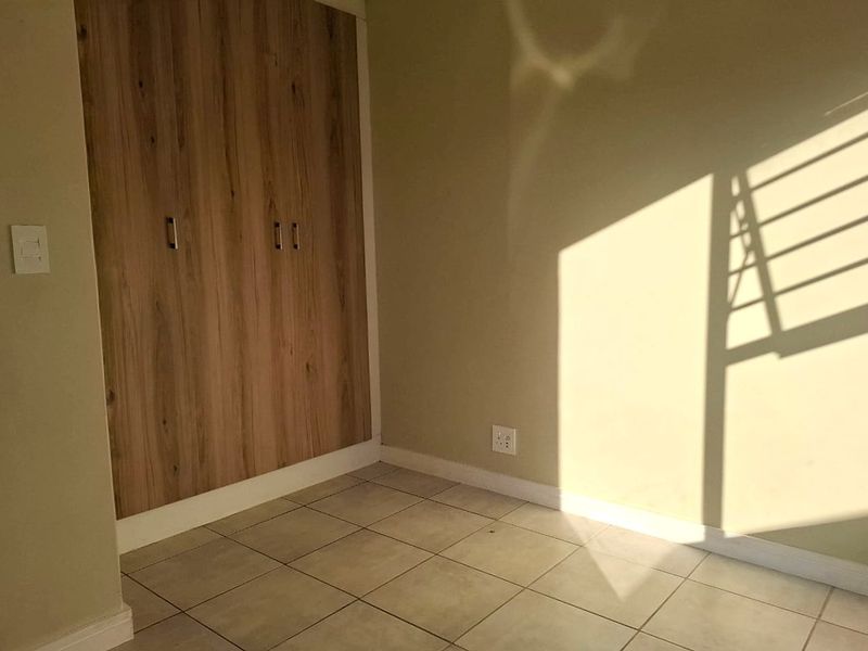 A bright, empty bedroom featuring neutral tiled flooring and modern wood-finish built-in cupboards, offering a clean and versatile space.