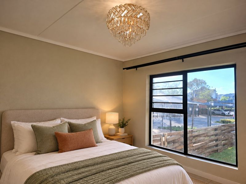 A well-lit bedroom featuring a modern black aluminium window frame and an elegant crystal chandelier, offering a comfortable and inviting living space.