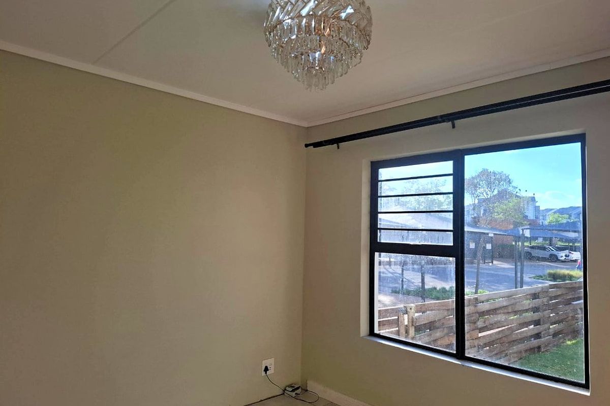 A bright, empty bedroom featuring tiled flooring, a large window with black metal frames, and a decorative ceiling light fixture.