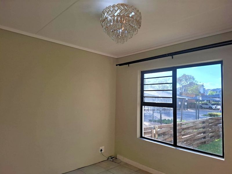 A bright, empty bedroom featuring tiled flooring, a large window with black metal frames, and a decorative ceiling light fixture.