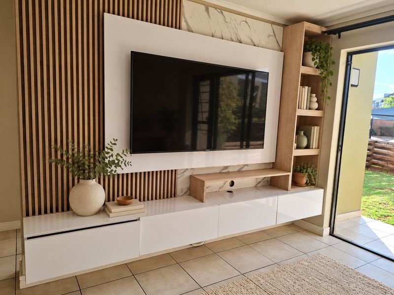 Modern living room featuring a custom built-in media unit with slatted timber accents, marble-effect wall cladding, and direct access to an outdoor patio area.