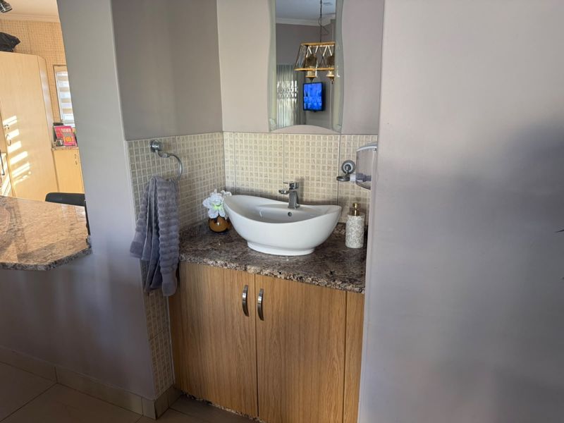 A compact bathroom vanity area featuring a modern vessel sink, granite countertop, wood-finish cabinetry, and a mosaic tile backsplash.