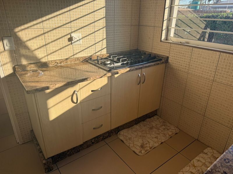 Compact kitchen area featuring granite countertops, built-in cabinetry, and a gas hob, finished with tiled splashbacks and flooring.