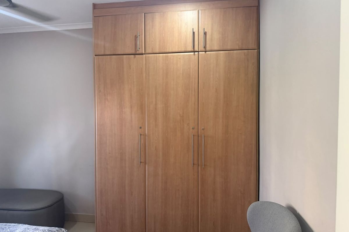 A bedroom featuring a large, floor-to-ceiling built-in wooden wardrobe with overhead storage compartments and a ceiling fan.