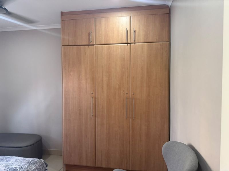 A bedroom featuring a large, floor-to-ceiling built-in wooden wardrobe with overhead storage compartments and a ceiling fan.