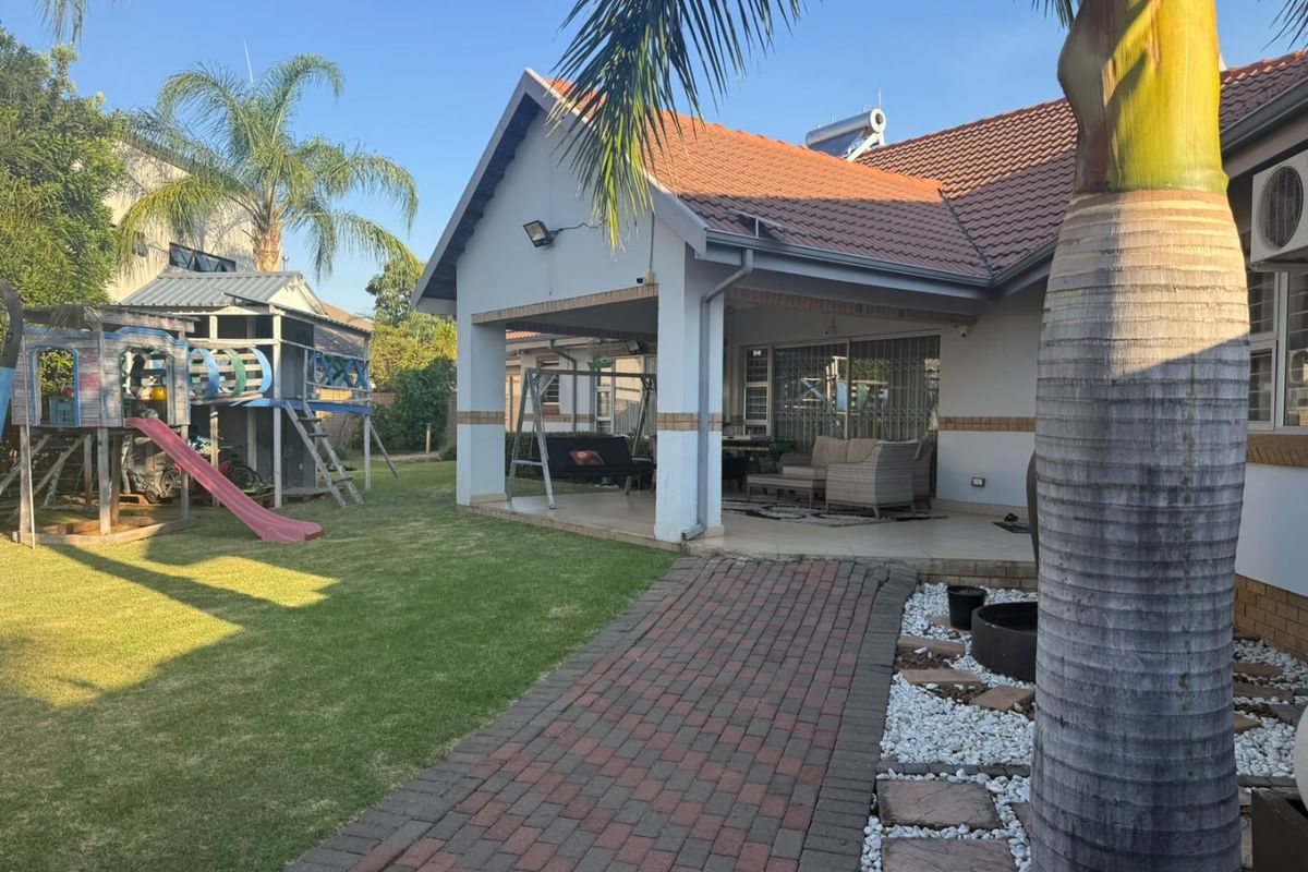 Rear view of the property featuring a covered patio, brick paved walkway, landscaped garden, and solar water heating system.