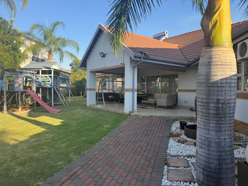 Rear view of the property featuring a covered patio, brick paved walkway, landscaped garden, and solar water heating system.