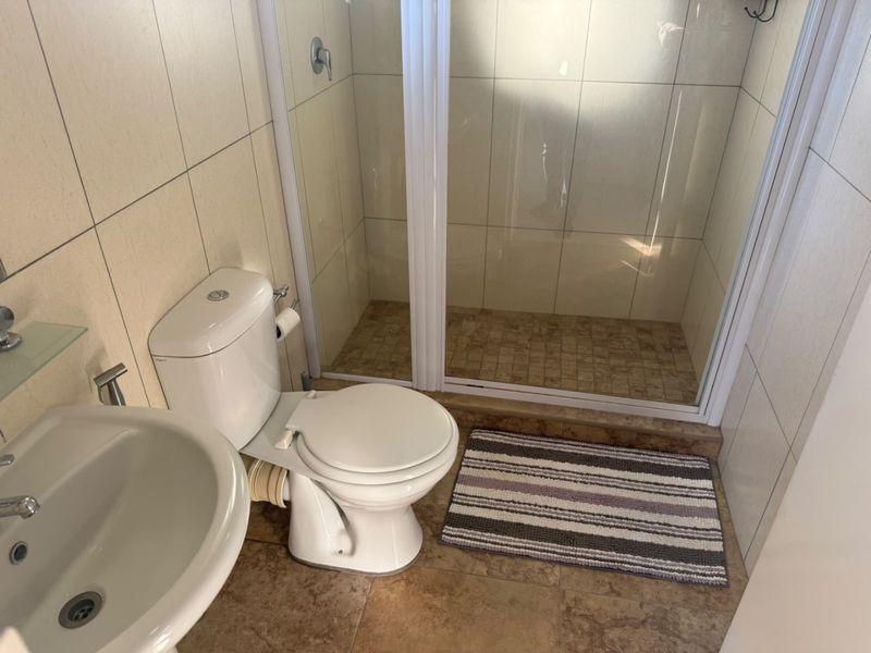 A functional bathroom featuring a pedestal basin, toilet, and a glass-enclosed shower with tiled walls and flooring.
