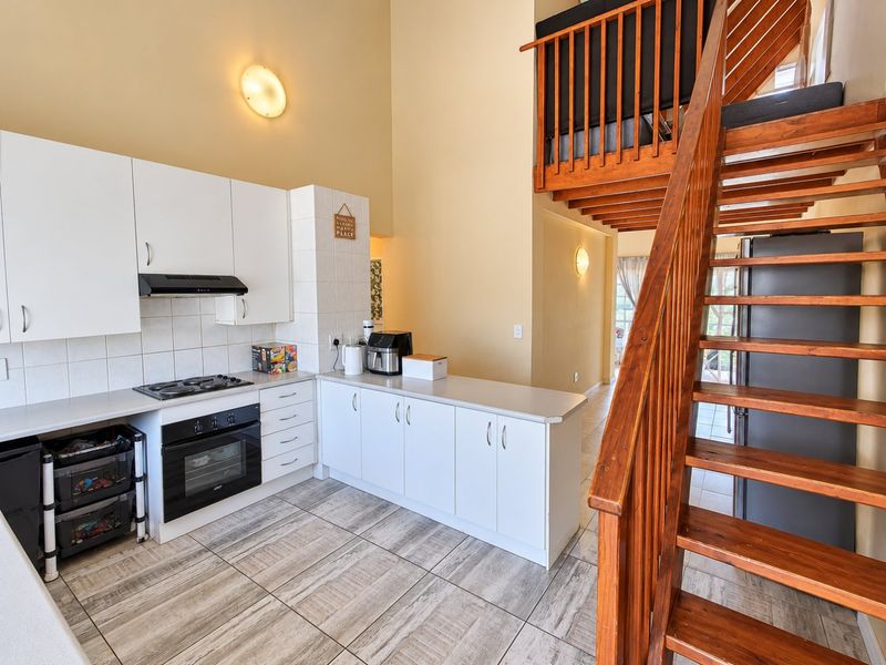 Open-plan kitchen featuring white cabinetry, built-in oven and hob, tiled flooring, and a wooden staircase leading to a mezzanine level.