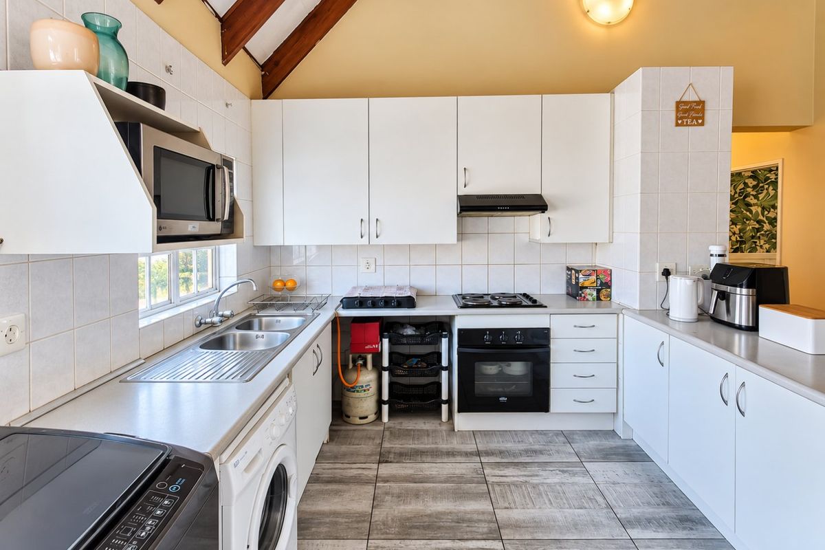 Functional kitchen featuring white cabinetry, built-in oven, gas hob, extractor fan, and tiled flooring under an exposed timber beam ceiling.