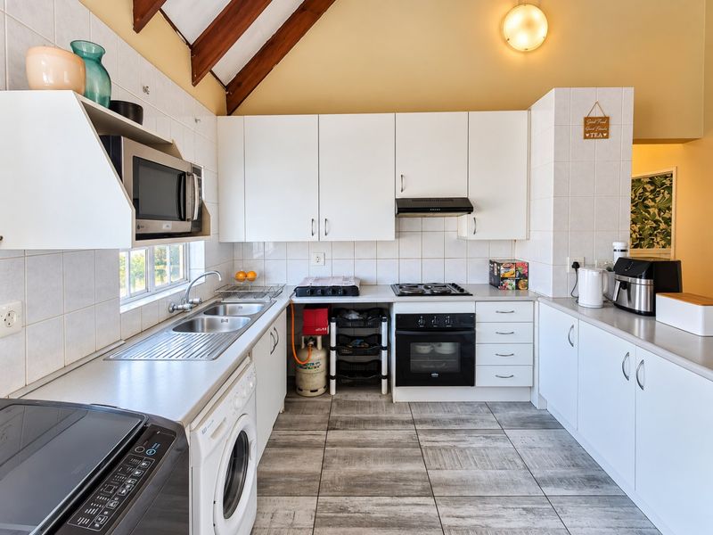 Functional kitchen featuring white cabinetry, built-in oven, gas hob, extractor fan, and tiled flooring under an exposed timber beam ceiling.