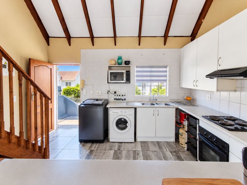 A functional kitchen featuring white cabinetry, built-in oven and hob, tiled backsplash, and exposed timber ceiling beams, with direct access to an outdoor area.