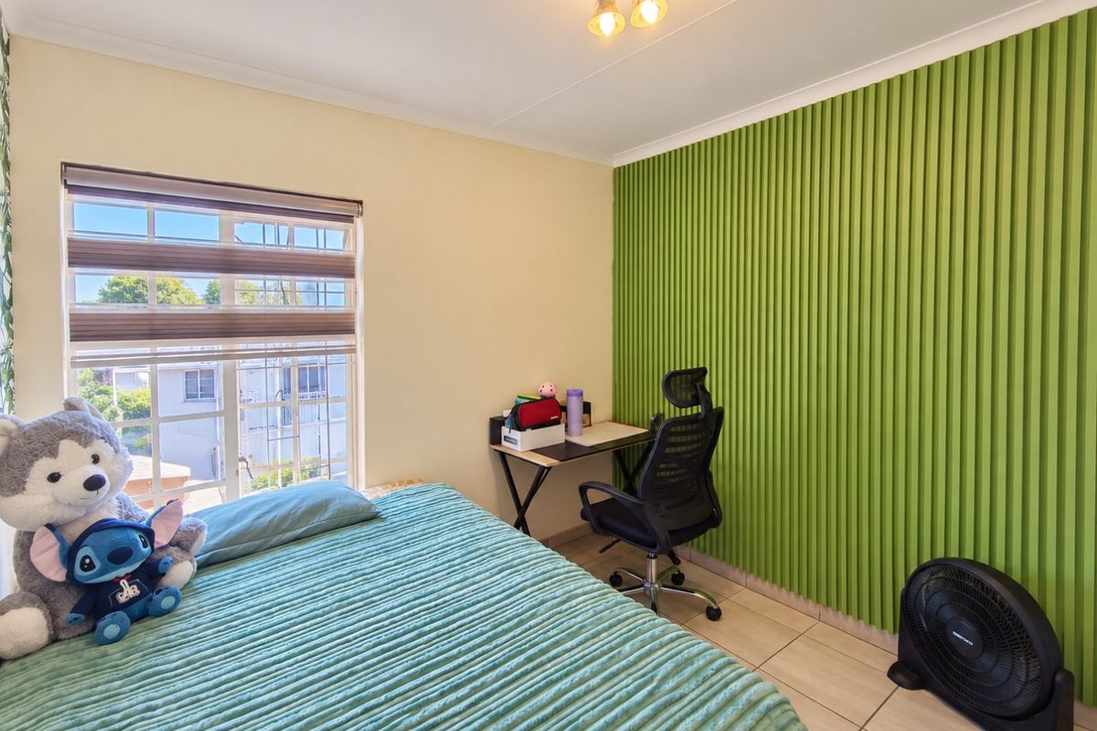 A bedroom featuring tiled flooring and a distinctive green decorative wall panel, complemented by a window with security bars and a ceiling light fixture.