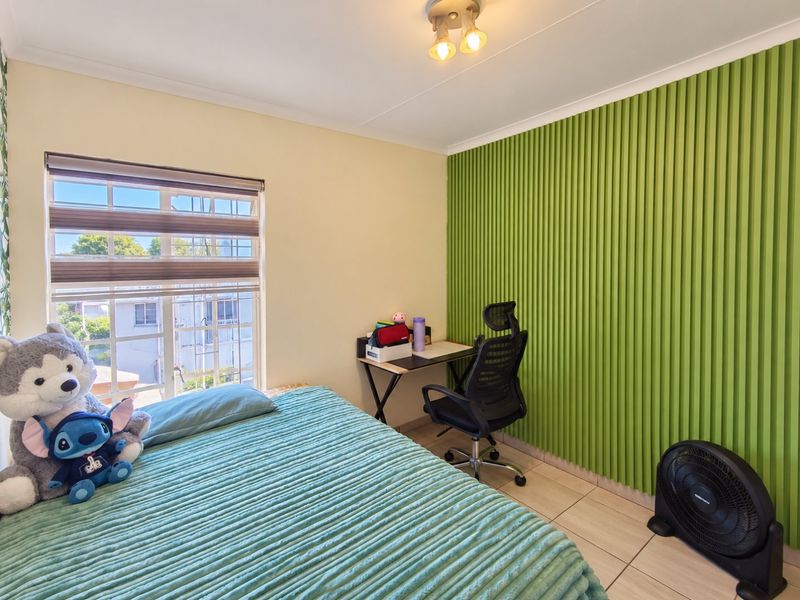 A bedroom featuring tiled flooring and a distinctive green decorative wall panel, complemented by a window with security bars and a ceiling light fixture.