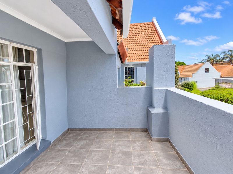 A clean, covered balcony featuring tiled flooring and a solid masonry balustrade, offering a private outdoor space with views of the surrounding complex.