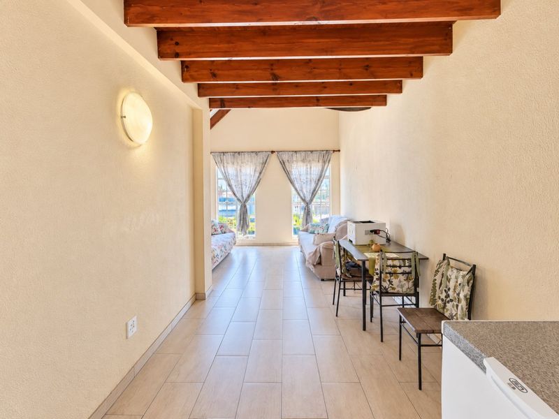 Open plan living area featuring exposed timber ceiling beams, tiled flooring, and natural light through double windows.
