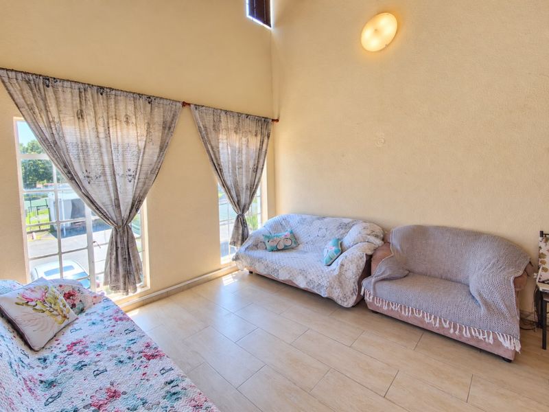 A bright living room featuring high vaulted ceilings, tiled flooring, and large windows that provide ample natural light.