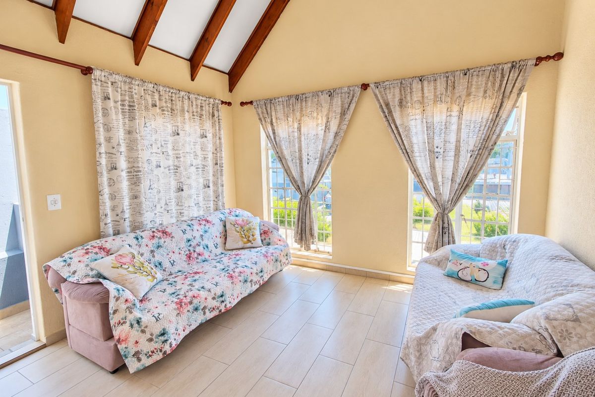 A bright living room featuring a high vaulted ceiling with exposed timber beams, tiled flooring, and large windows that provide ample natural light.