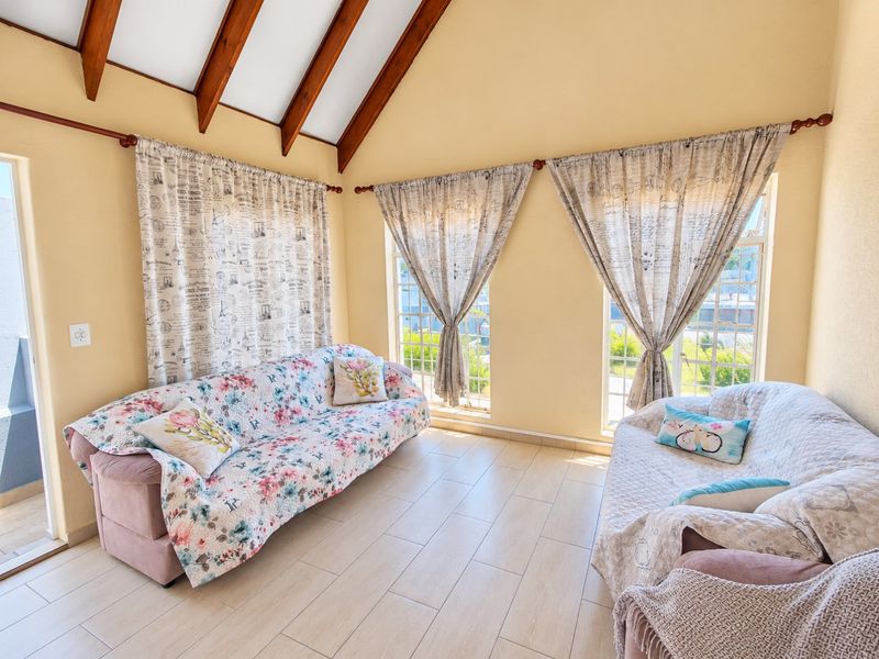 A bright living room featuring a high vaulted ceiling with exposed timber beams, tiled flooring, and large windows that provide ample natural light.