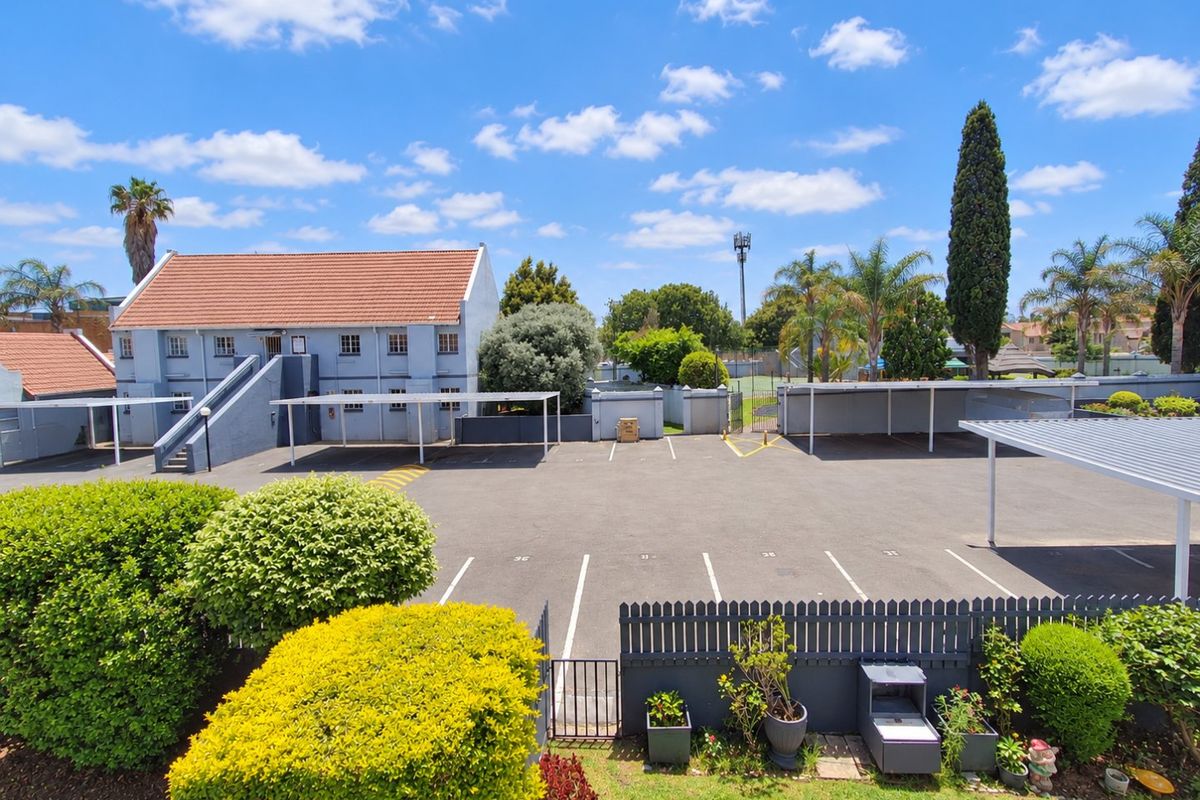 An elevated view of the apartment complex rear parking area, featuring covered carports, paved parking bays, and well-maintained landscaped garden borders.