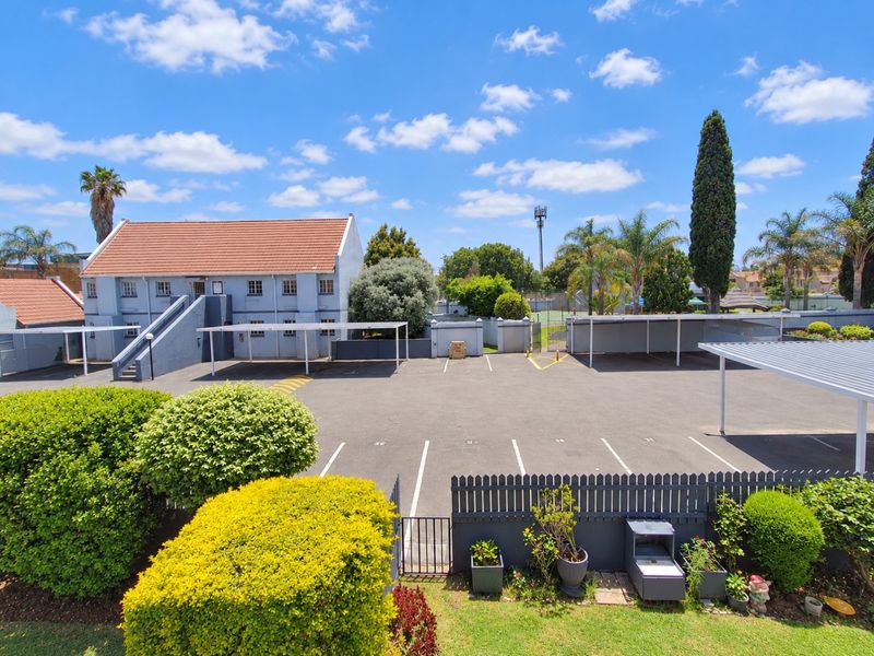 An elevated view of the apartment complex rear parking area, featuring covered carports, paved parking bays, and well-maintained landscaped garden borders.