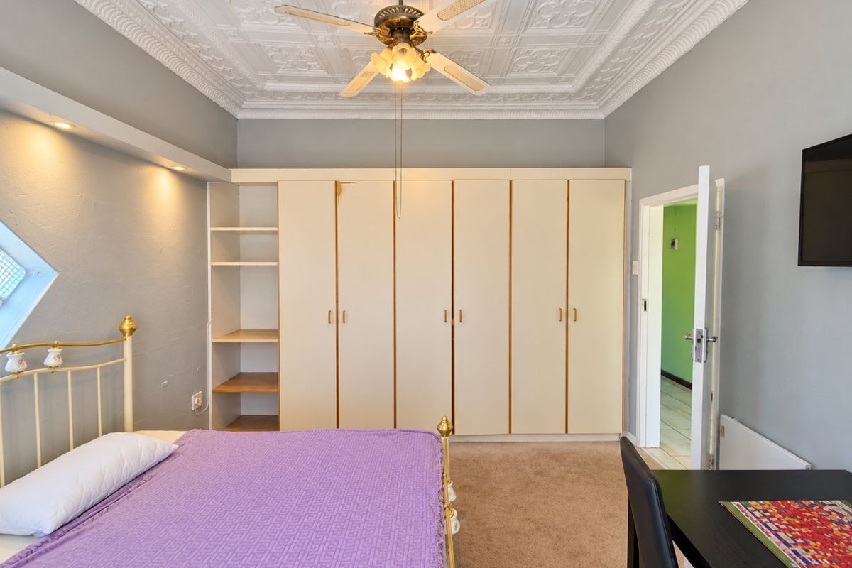 A bedroom featuring built-in cupboards, decorative ceiling tiles with a fan, and recessed lighting, offering a functional space with potential for cosmetic updates.