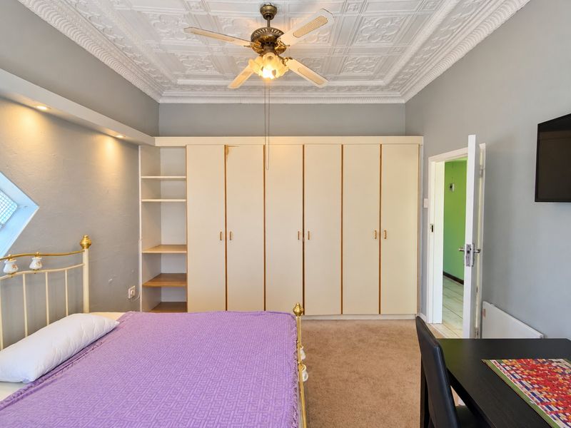 A bedroom featuring built-in cupboards, decorative ceiling tiles with a fan, and recessed lighting, offering a functional space with potential for cosmetic updates.