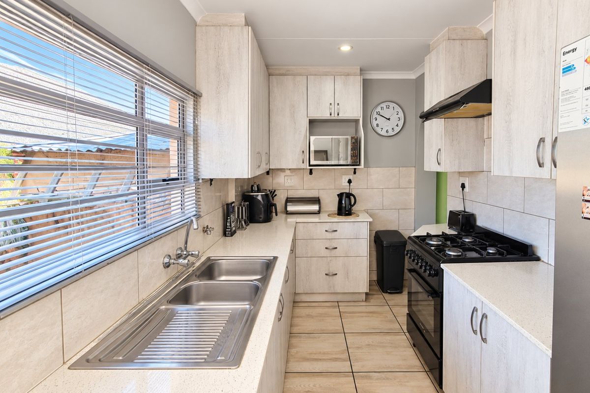 A well-maintained kitchen featuring light wood-grain cabinetry, a double stainless steel sink, gas stove with extractor fan, and neutral tiled splashbacks.
