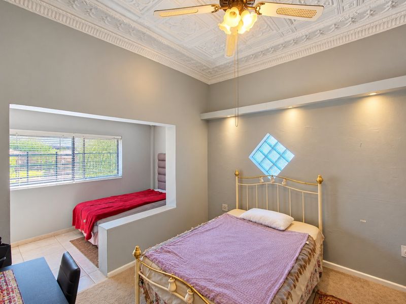 A bedroom featuring decorative ceiling molding, a ceiling fan, and a unique glass block window, with a partitioned sleeping area.