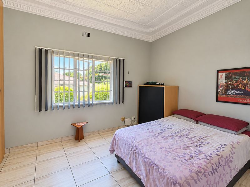 A bedroom featuring tiled flooring, an ornate ceiling cornice, and a window fitted with security bars and vertical blinds.
