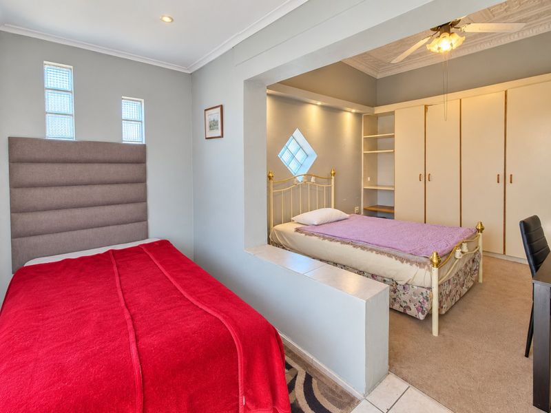 Spacious bedroom featuring built-in cupboards, decorative ceiling coving, recessed lighting, and unique glass block windows, offering a functional layout with a partitioned sleeping area.