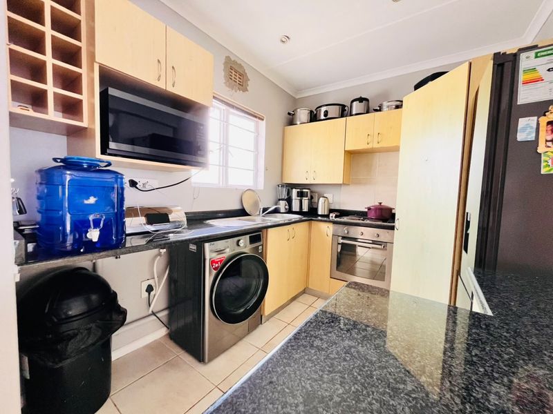 Compact kitchen featuring light wood cabinetry, granite countertops, built-in oven, and integrated laundry facilities, offering a functional layout for apartment living.