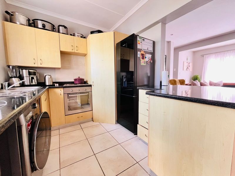 Functional kitchen featuring light wood cabinetry, granite countertops, built-in oven, and tiled flooring, with an open-plan layout connecting to the living area.