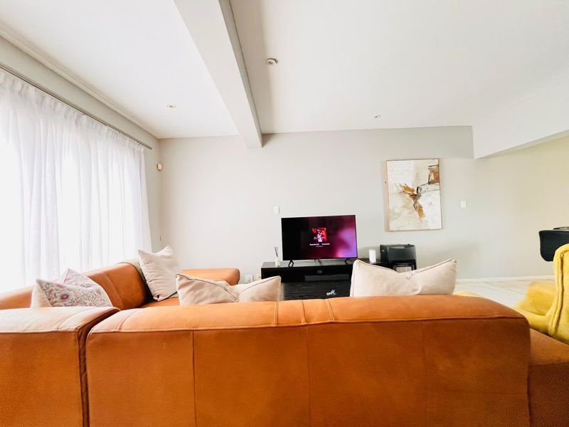 A bright and spacious living room featuring neutral walls, recessed downlighting, and an exposed ceiling beam, creating a comfortable and inviting atmosphere.