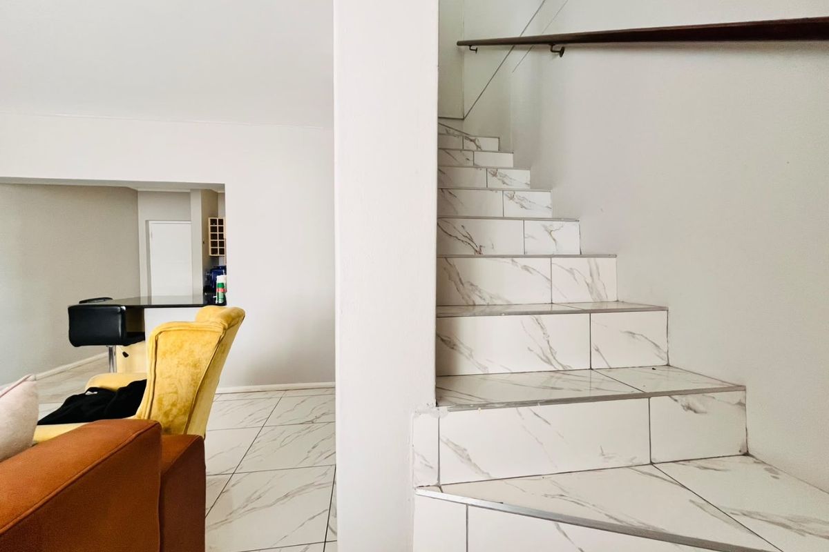 A bright living area featuring modern marble-look floor tiles and a matching tiled staircase with a sleek wall-mounted handrail.