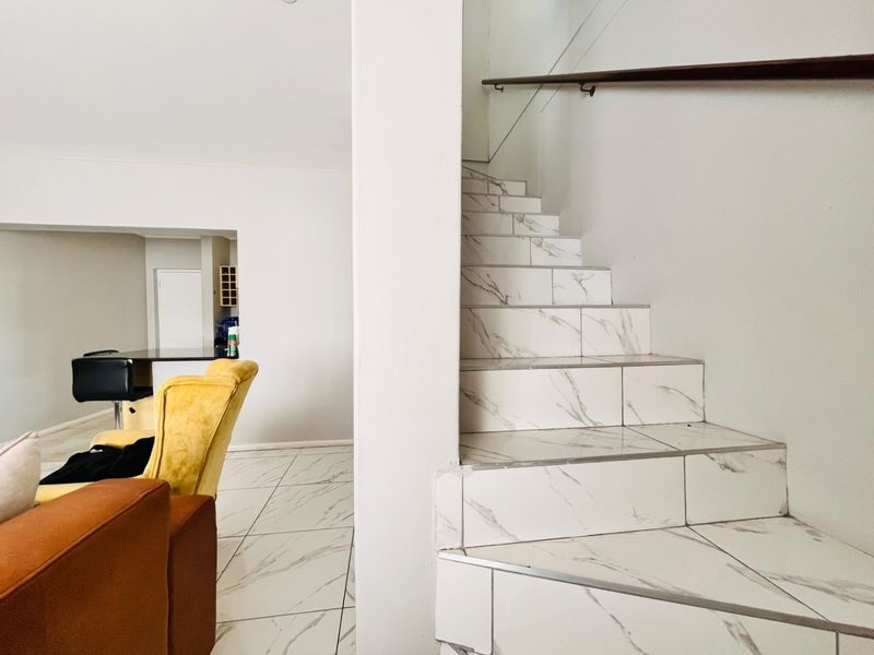 A bright living area featuring modern marble-look floor tiles and a matching tiled staircase with a sleek wall-mounted handrail.