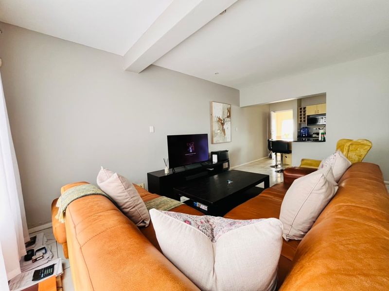 An open-plan living area featuring tiled flooring, recessed lighting, and a functional kitchen with a breakfast bar, creating a cohesive and versatile living space.