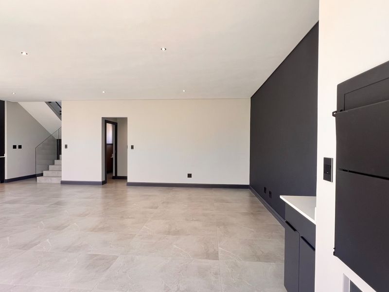 Spacious open-plan living area featuring modern porcelain floor tiles, recessed lighting, and a sleek staircase with glass balustrade, offering a clean contemporary aesthetic.