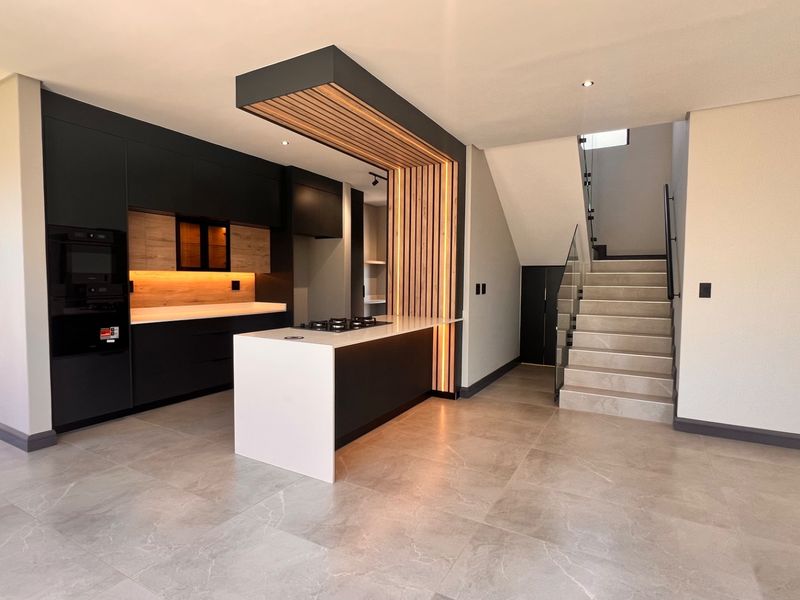 Modern open-plan kitchen featuring sleek dark cabinetry, a central island with integrated hob, and a striking timber slat feature, adjacent to a contemporary staircase.